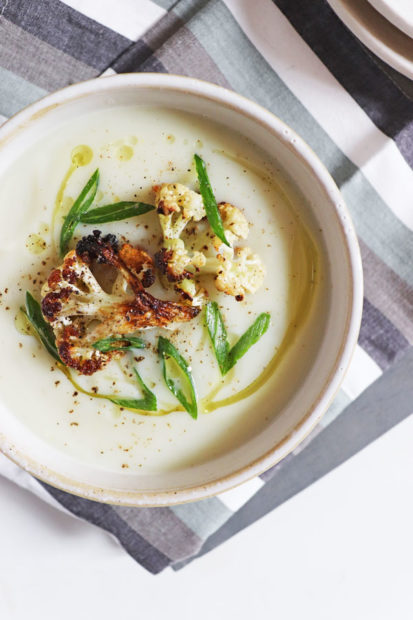 Bowl of creamy roasted cauliflower soup, topped with cauliflower florets, olive oil, scallions and black pepper