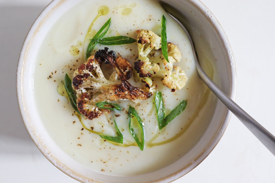 Bowl of creamy roasted cauliflower soup, topped with cauliflower florets, olive oil, scallions and black pepper