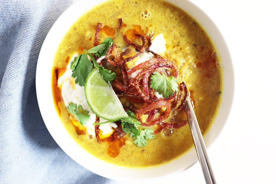 A bowl of spiced lentil soup made with red lentils, topped with yogurt, onions, fresh coriander and a wedge of lime