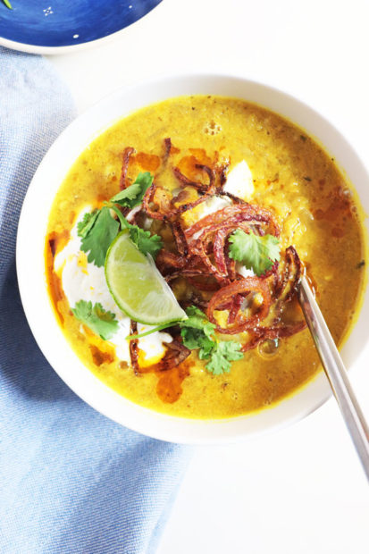 A bowl of spiced lentil soup made with red lentils, topped with yogurt, onions, fresh coriander and a wedge of lime
