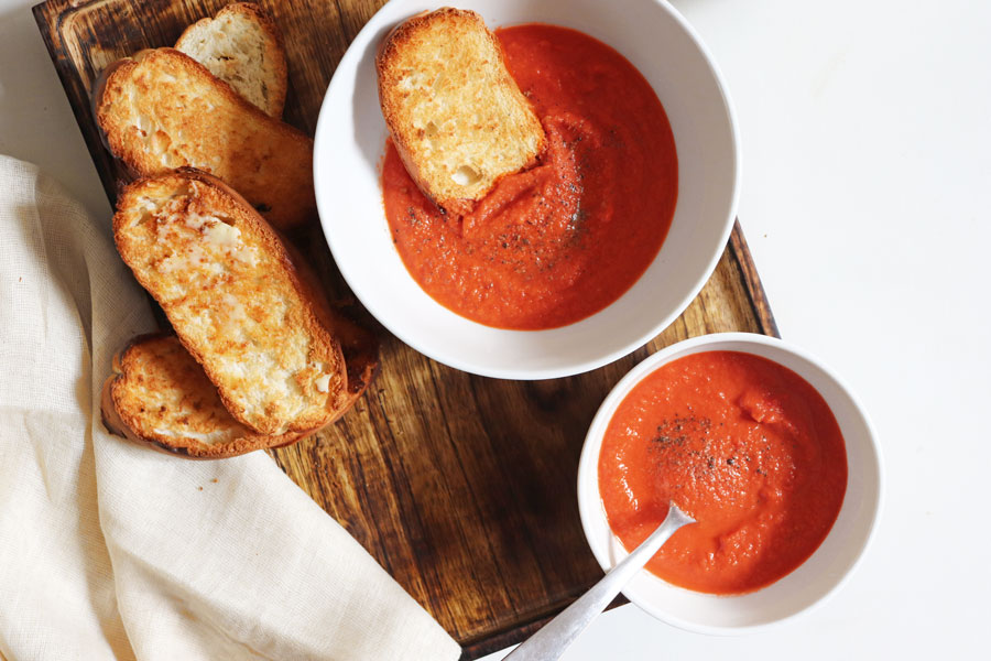 Two bowls of creamy oven roasted tomato soup with a side of garlic bread