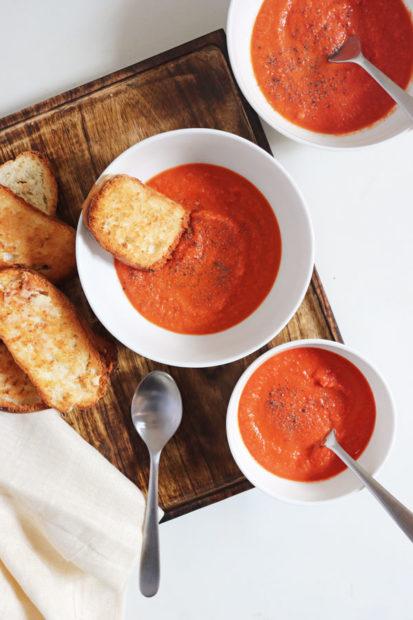 Two bowls of creamy oven roasted tomato soup with a side of garlic bread