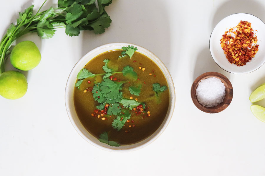 A bowl of vegan bone broth with herbs, limes, chilli