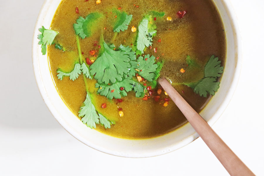 A bowl of vegan bone broth with herbs and chilli