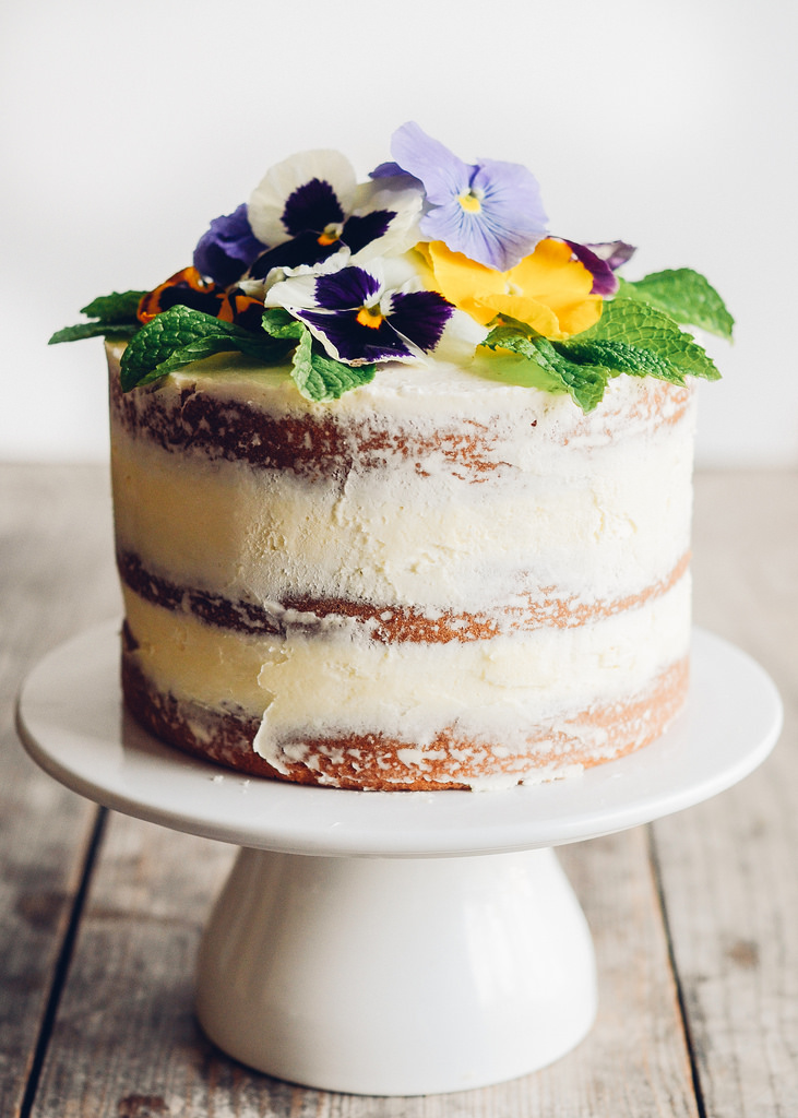 A naked vanilla cake with edible flowers as decoration
