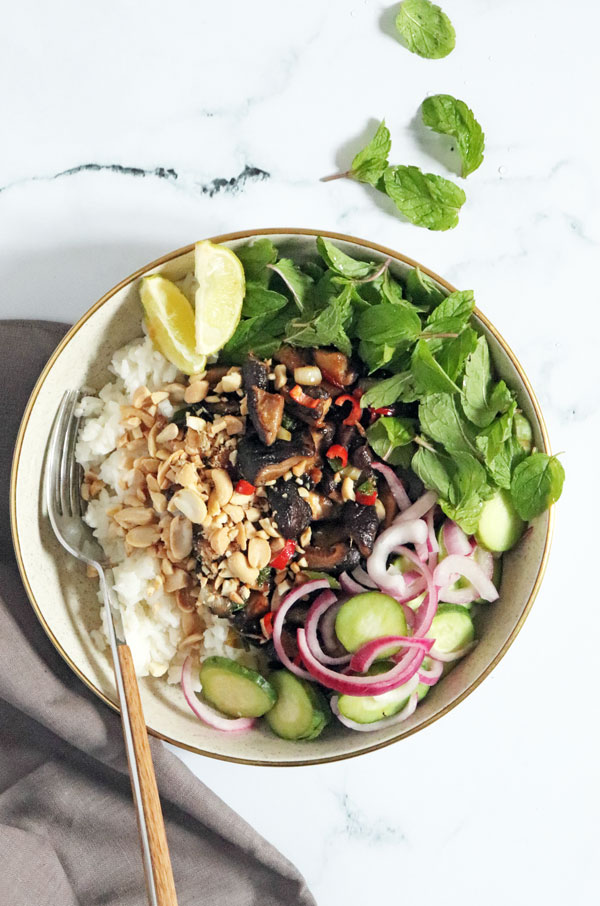 Bowl of coconut rice with mushroom larb, herbs, pickled onions and lime wedges